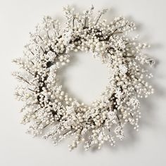 a wreath with white flowers and branches on a white background, the center piece is surrounded by small beads