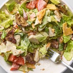 a white bowl filled with lettuce, tomato and meat salad next to a fork