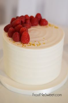 a white cake with raspberries on top is sitting on a plate and has gold sprinkles