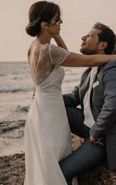 a man and woman sitting on the beach next to each other with their arms around one another