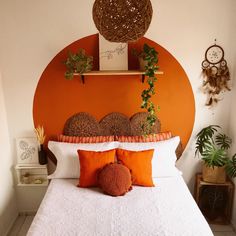 a bed with an orange headboard and white bedspread is decorated with potted plants