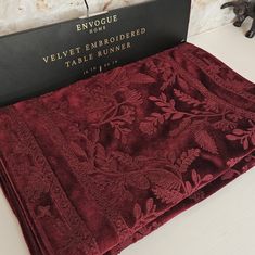 the table cloth is red and has gold trimmings on it, along with a black box that says velvet embroidered table runner