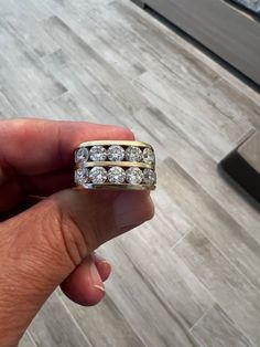 a hand holding a gold ring with three rows of diamonds on it, in front of a tile floor