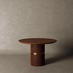 a round wooden table sitting on top of a white floor next to a gray wall