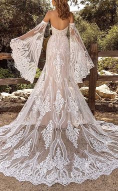 a woman in a white wedding dress with sheer sleeves and an open back, standing near a fence