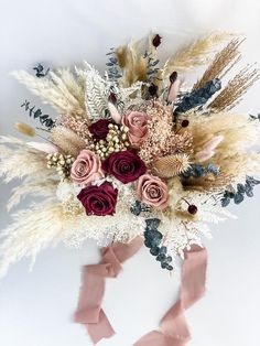 an arrangement of dried flowers and feathers on a white background with pink ribbon tied around it