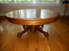 a round wooden table sitting on top of a hard wood floor next to a window