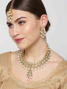 This stunning jewelry set consists of a classic drop necklace, a maang tikka, and a pair of matching drop earrings. The gold toned & off-white pearl necklace with a central drop shown here comes with kundan stone studs & beads, is gold-plated, and secured with an adjustable drawstring closure. A pair of matching drop earrings come secured with a post and back closure. This beautiful statement piece can add impact to any outfit for any festive occasion! Product color may vary based on the monitor Gold Kundan Jewelry Sets With Pearl Drop, Kundan Chandbali Jewelry Set With Pearl Drop, Bollywood Kundan Bridal Necklace With Pearl Drop, Kundan Chandbali Necklace With Pearl Drop, Chandbali Kundan Necklace With Pearl Drop, Temple Jewelry Sets With Pearl Drop For Festive Occasions, Temple Jewelry Sets With Pearl Drop For Festive Season, Gold Bridal Necklace With Pearl Drop For Diwali, White Kundan Jewelry Sets