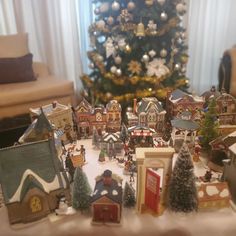 a christmas tree is in the background with many small houses and trees around it on a table