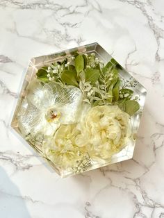 some flowers are in a glass vase on a marble counter top with green leaves and buds