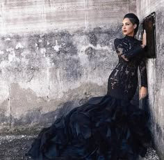 a woman in a black dress leaning against a wall