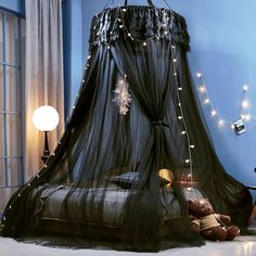 a black canopy bed with lights hanging from it's sides and a teddy bear on the floor