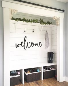 a welcome sign is mounted on the side of a white wall with baskets under it