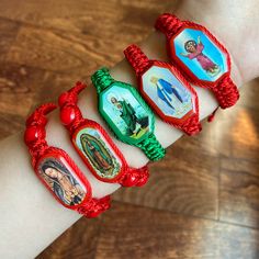 four bracelets with pictures on them sitting on top of a wooden table next to a person's hand