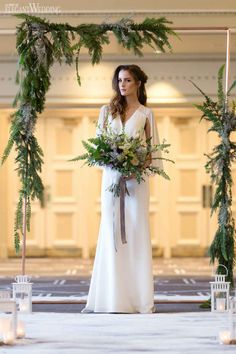 a woman standing in front of a wedding arch with greenery and flowers on it