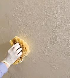 a person in white gloves with a yellow duster on their hand and a sponge on the wall