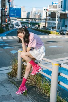 a young woman sitting on a fence next to a street with buildings in the background