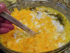 someone is mixing cheese in a bowl with a wooden spoon