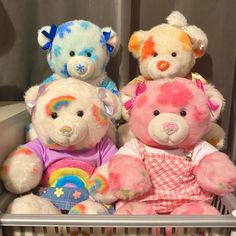 three teddy bears are sitting in a basket with their faces painted pink, blue, yellow and orange