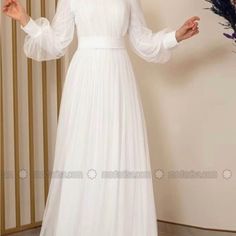 a woman in a long white dress standing next to a plant and holding her hands out