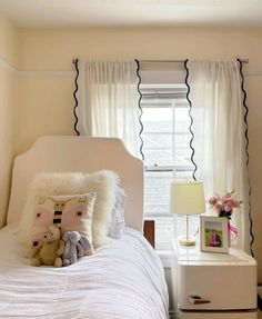 a white bed sitting under a window next to a nightstand with a stuffed animal on it