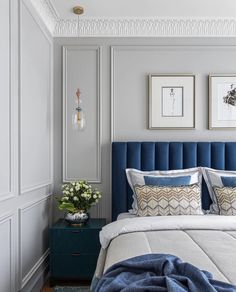 a bed with blue headboard and pillows in a white walled room next to two framed pictures on the wall