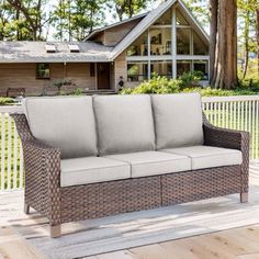 a wicker couch sitting on top of a wooden deck next to a house and trees