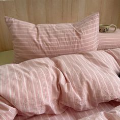 a bed with pink and white striped sheets, pillows and a black cat laying on it