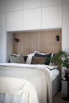 a bed with white sheets and pillows next to a plant in a vase on a table