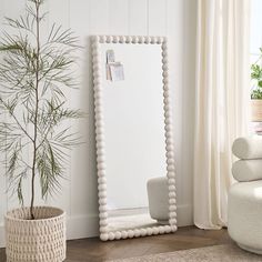 a white mirror sitting on top of a wooden floor next to a potted plant