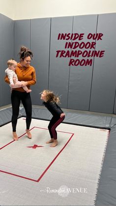 two women and a baby on a trampoline in a room with gray walls