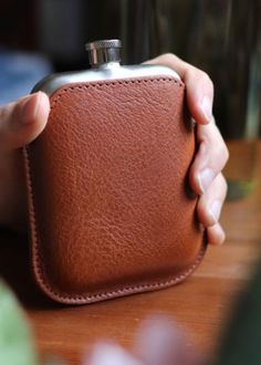 a person holding a brown leather flask case