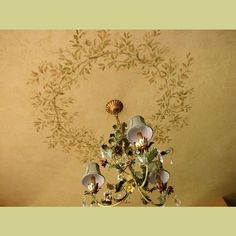 a chandelier hanging from the ceiling in front of a wall with leaves and flowers painted on it