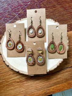 four wooden earrings with flowers and leaves are displayed on a piece of wood that is sitting on a table