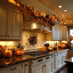 a kitchen filled with lots of white cabinets and counter tops covered in fall leaves hanging from the ceiling