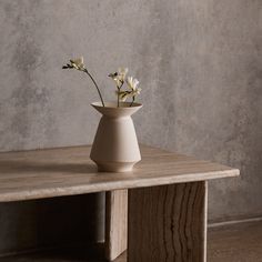 a white vase with flowers sitting on top of a wooden table in front of a concrete wall