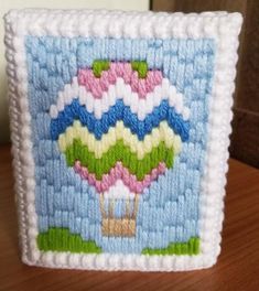 a needle - embroidered picture of a hot air balloon in the sky on a wooden table