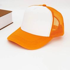 an orange and white trucker hat next to a book on a white table top