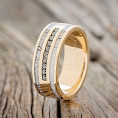 a wedding ring with white and yellow gold inlays on it sitting on a piece of wood