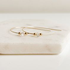 Add a touch of sparkle to your everyday outfits with our Herkimer Diamond Open Hoop Earrings. Made from one continuous 14K gold filled thread, these earrings feature a sleek, double-pointed crystal accented with tiny gold spheres. A subtle statement piece that is comfortable and easy to wear. (No need to be a gemologist to rock these!) -- Herkimer crystals measure approximately 5-7mm 14K gold filled approximate length: 1.75" Herkimer “diamonds” are affectionately named for the Herkimer County in NY where they were first discovered and mined. While not true diamonds, Herkimer crystals are like diamonds due to their clear, sparkly, and faceted characteristics. Elegant Herkimer Diamond Crystal Necklaces For Gifts, Herkimer Diamond Wire Wrap, Elegant Herkimer Diamond Crystal Necklace Gift, Herkimer Diamond Jewelry, Herkimer Diamond Earrings, Hoop Charms, Open Hoop Earrings, Pearl Gemstone, Pearl Wedding