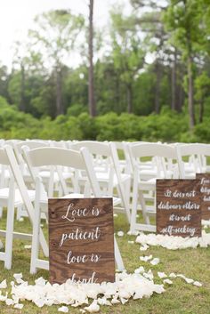 the chairs are set up for an outdoor ceremony with white petals on the ground and wooden signs that read love is patient love is kind