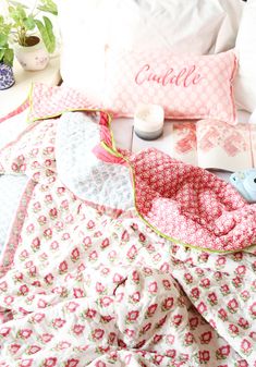 a bed with pink and white sheets, pillows and other items on it next to a potted plant