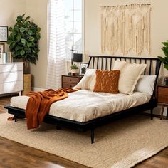 a bed sitting on top of a wooden floor next to a white dresser and potted plant