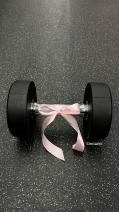 a pair of black dumbbells with pink ribbon tied around them on the floor