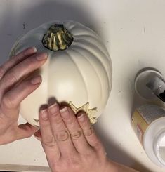 two hands are reaching for a white pumpkin on the counter top, while another hand holds it up