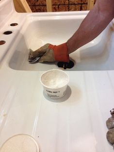 a person in orange gloves is painting a white sink