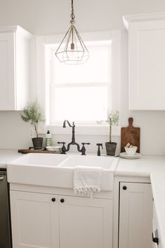 a kitchen with white cabinets and black faucet in the sink, along with potted plants