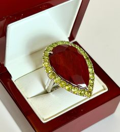 An large pear cut red Ruby surrounded with 24 round cut green Peridot.  All natural multi gemstones ring.  The Ring has been hand crafted in 92.5 silver with UK hallmark. It has a smooth and polish finish with a  modern contemporary ring.  Ruby Clarity -  Opaque Colour           - Red Type              - Natural Ruby Peridot Clarity - Transparent Colour              - Sparkling  Green Type                  - Natural Peridot Oval Ruby Stone Measurement :  28.4mm Length x 18.7mm Width x 8.9mm Depth Round Peridot Stones Measurement : 3.5mm Length, 16 stones Ring measurements : 37mm Length x 27mm Width x 11.3mm Depth of stone sit on the finger   Ring size :  UK Q ½, US 8 ½; Total ring weight : 17.9 grams Ring band width : 3.7 mm  approx. Ring band thickness : 2 mm approx. 92.5 Sterling Silver Colored Stone Rings, Multi Gemstone Ring, Purple Amethyst Ring, Ring Ruby, Contemporary Ring, Peridot Stone, Ruby Stone, Green Peridot, Valentines Jewelry