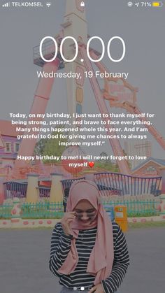 a woman wearing a hijab standing in front of a carnival ride and texting on her phone