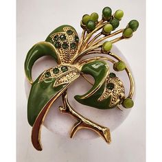 a brooch with green beads and leaves on it's back, sitting on a white surface